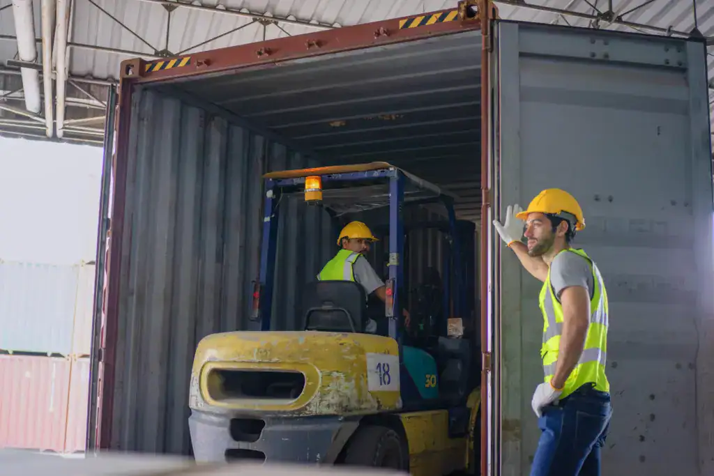 Workers use a forklift to load goods into a shipping container for order processing and shipment management.